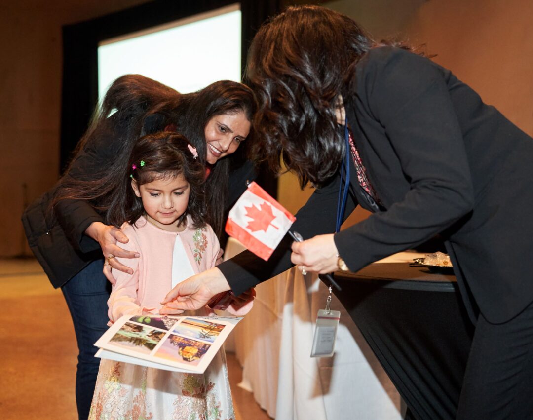 Adults showing a child a booklet while holding a Canadian flag.