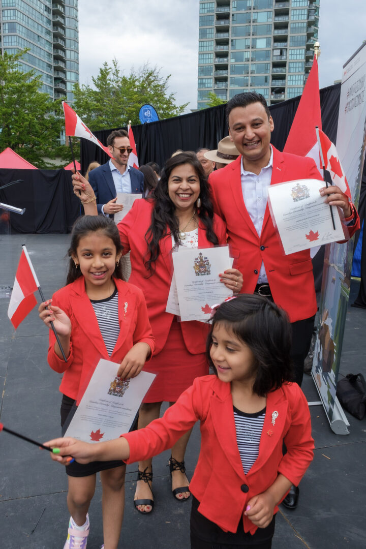A family holding their Canadian citizenship certificates while waving Canadian flags.